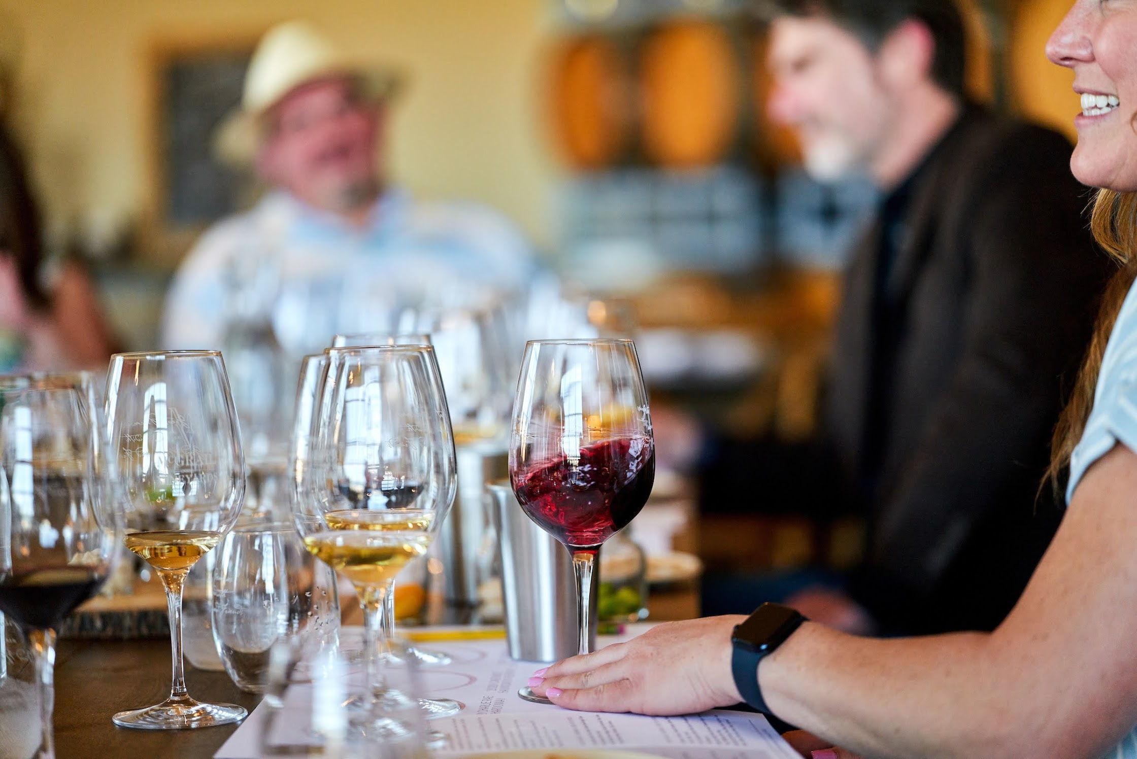 Wine glasses with red and white wines at a tasting event with guests in the background.