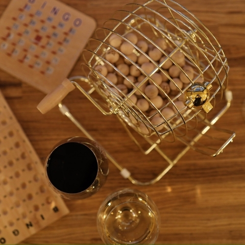 Bingo cage, bingo cards, and glasses of red and white wine set on a wooden table for Barrels and Bingo at McGrail Vineyards.