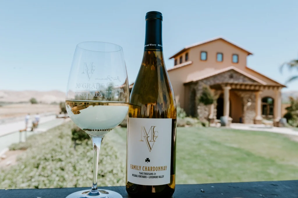 McGrail Family Chardonnay bottle and glass with vineyard building in background.