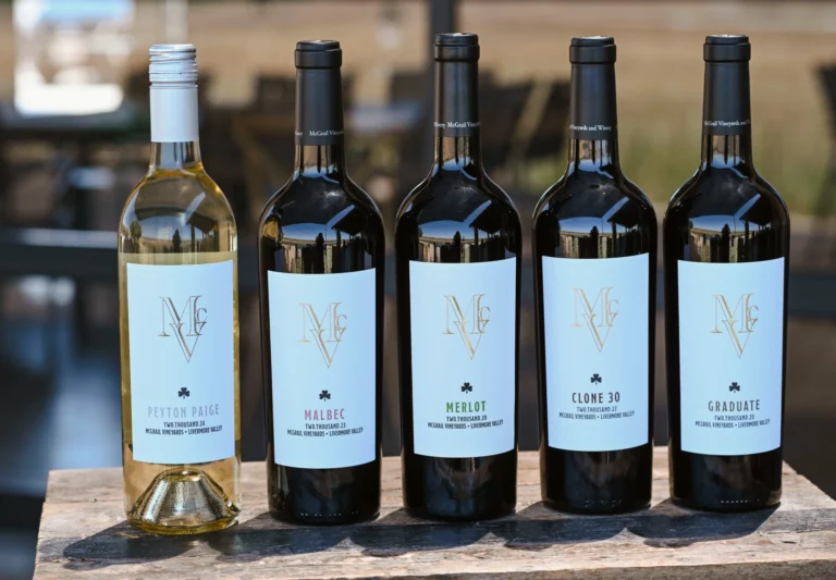 McGrail wine bottles lined up outdoors, including Sauvignon Blanc, Malbec, Merlot, Clone 30, and Graduate.