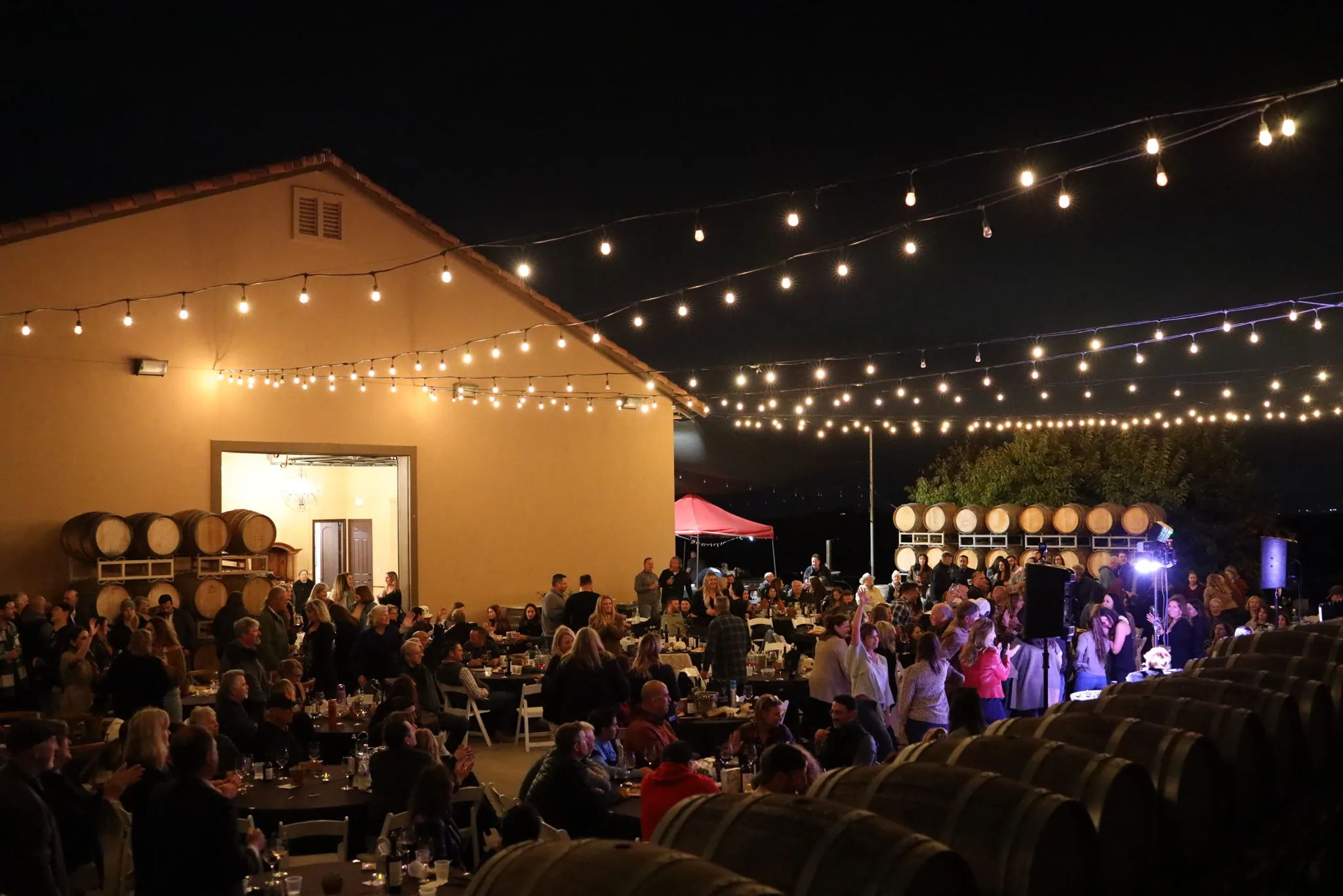 Nighttime vineyard event with guests dining under string lights at McGrail Vineyard buildings.
