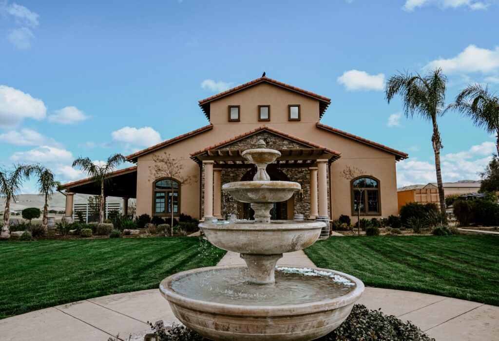 McGrail Vineyards winery with landscaped lawn, fountain, palm trees, and vineyard views under a clear blue sky.