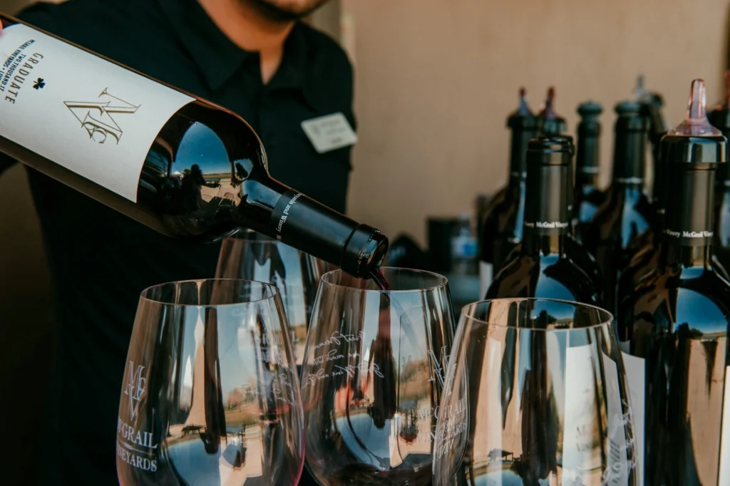 Red wine being poured from a labeled bottle into a branded wine glass during a tasting event.