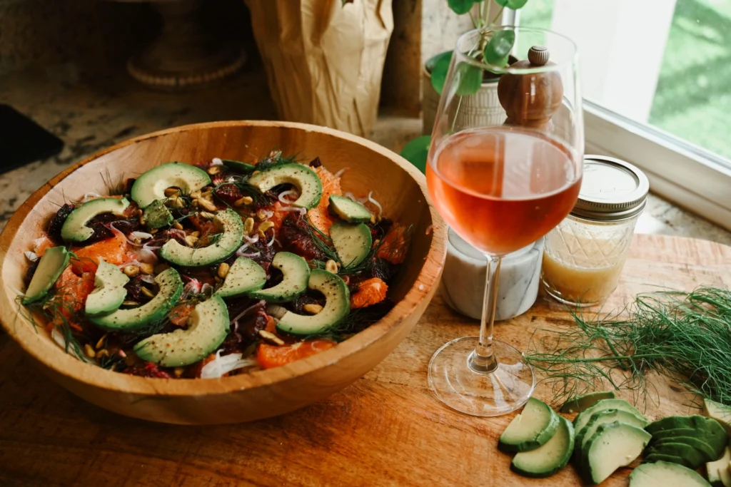 Fresh vegetable salad in a wooden bowl with rosé wine and condiments on the table. 