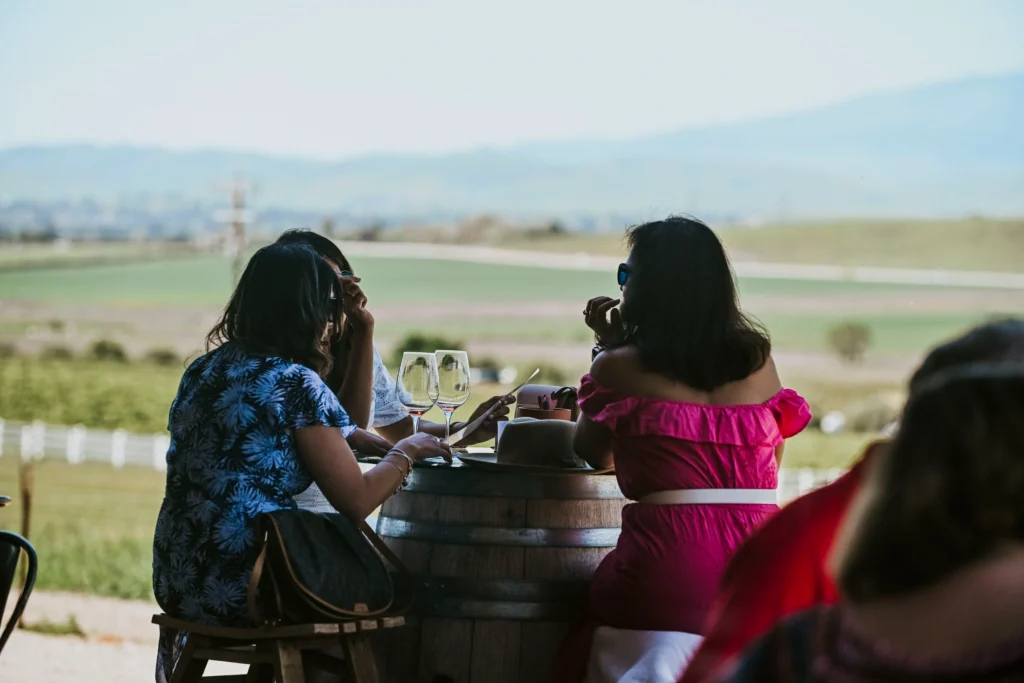 Women enjoying wine tasting at a vineyard patio with countryside views.