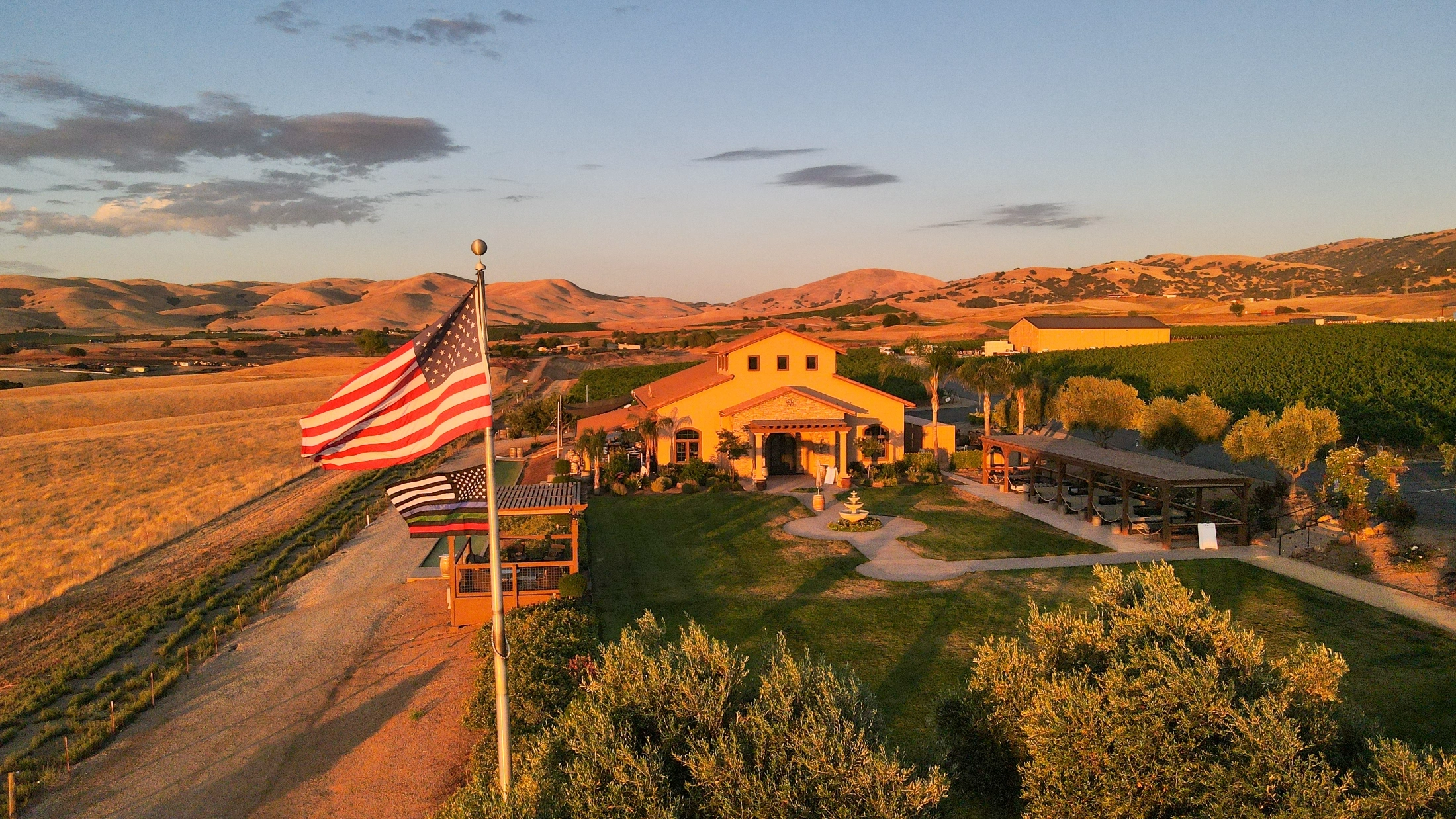 Yellow winery building with arches and American flag overlooking McGrail Vineyard's rolling terrain at sunset.