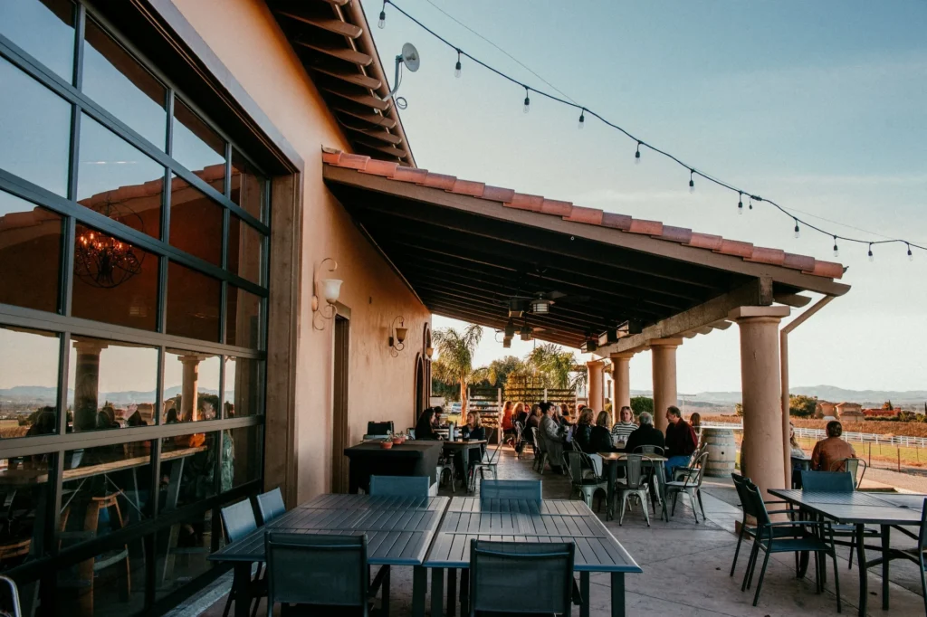 Covered patio at McGrail Vineyard with pergola, string lights, and guests seated at tables overlooking vineyard landscape.