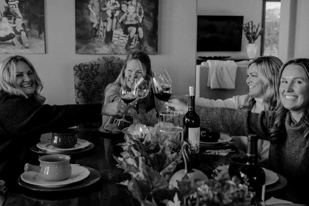 Four women toasting with wine glasses at a dining table during a social gathering.