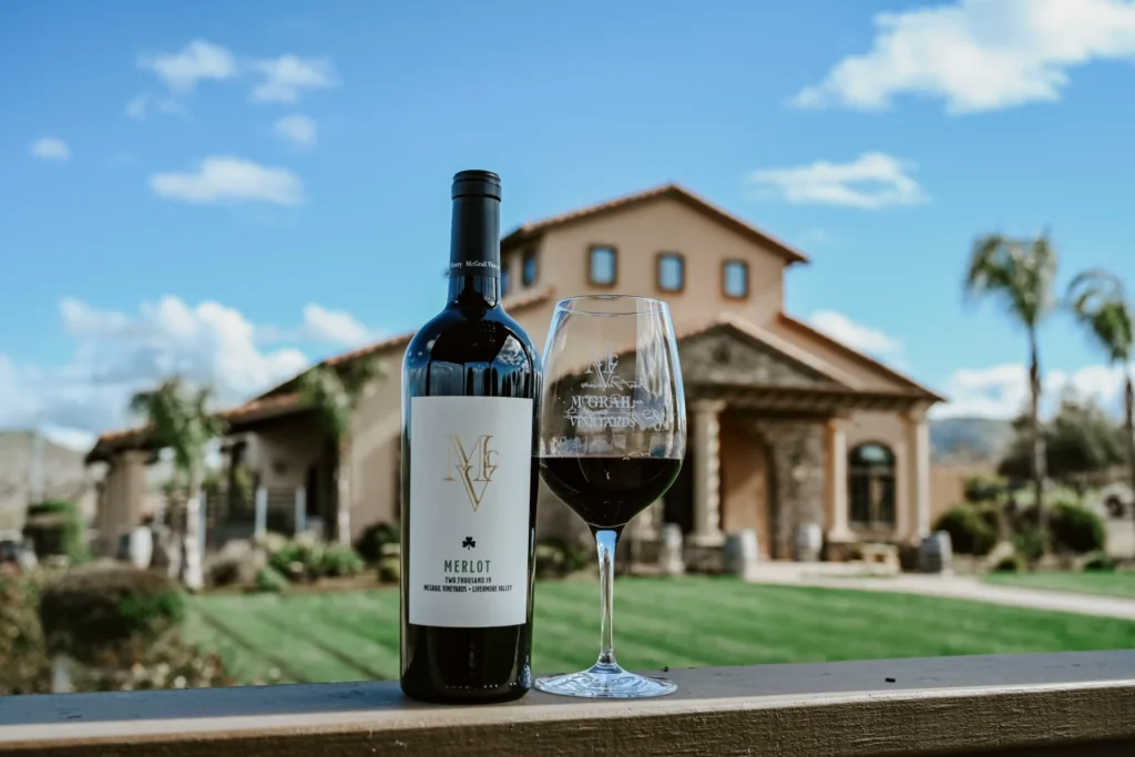 Merlot wine bottle and glass with McGrail Vineyard villa in background.
