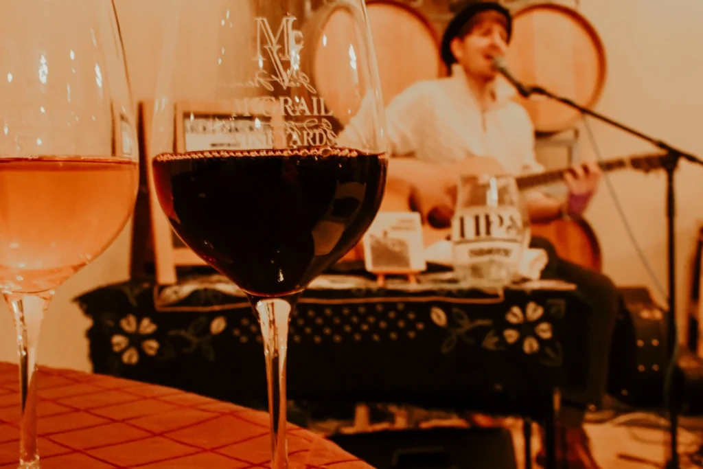 Red wine glass in focus with musician performing guitar in background at a McGrail Vineyard wine event.